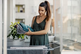 Hausarbeit und schwangere Frauen. Die Frau legt die Handtücher nach dem Trocknen an einem sonnigen Tag auf die Terrasse. Sie hält ordentlich gefaltete Handtücher in der einen Hand, während sie mit der anderen ihren Bauch hält