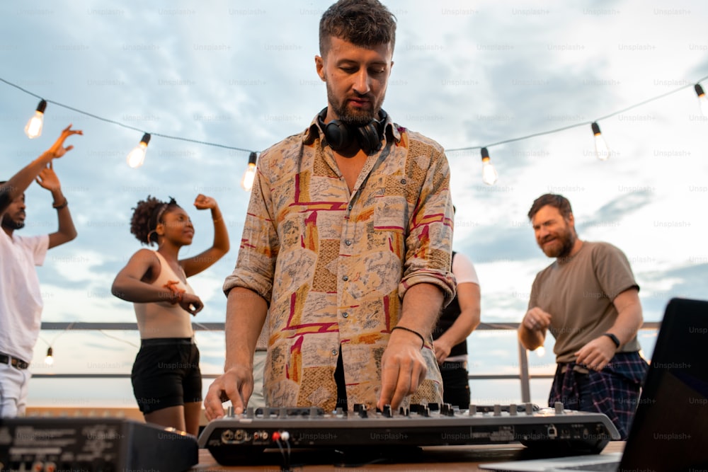 Junger DJ mit Kopfhörern um den Hals, der am Resonanzboden vor tanzenden Freunden steht