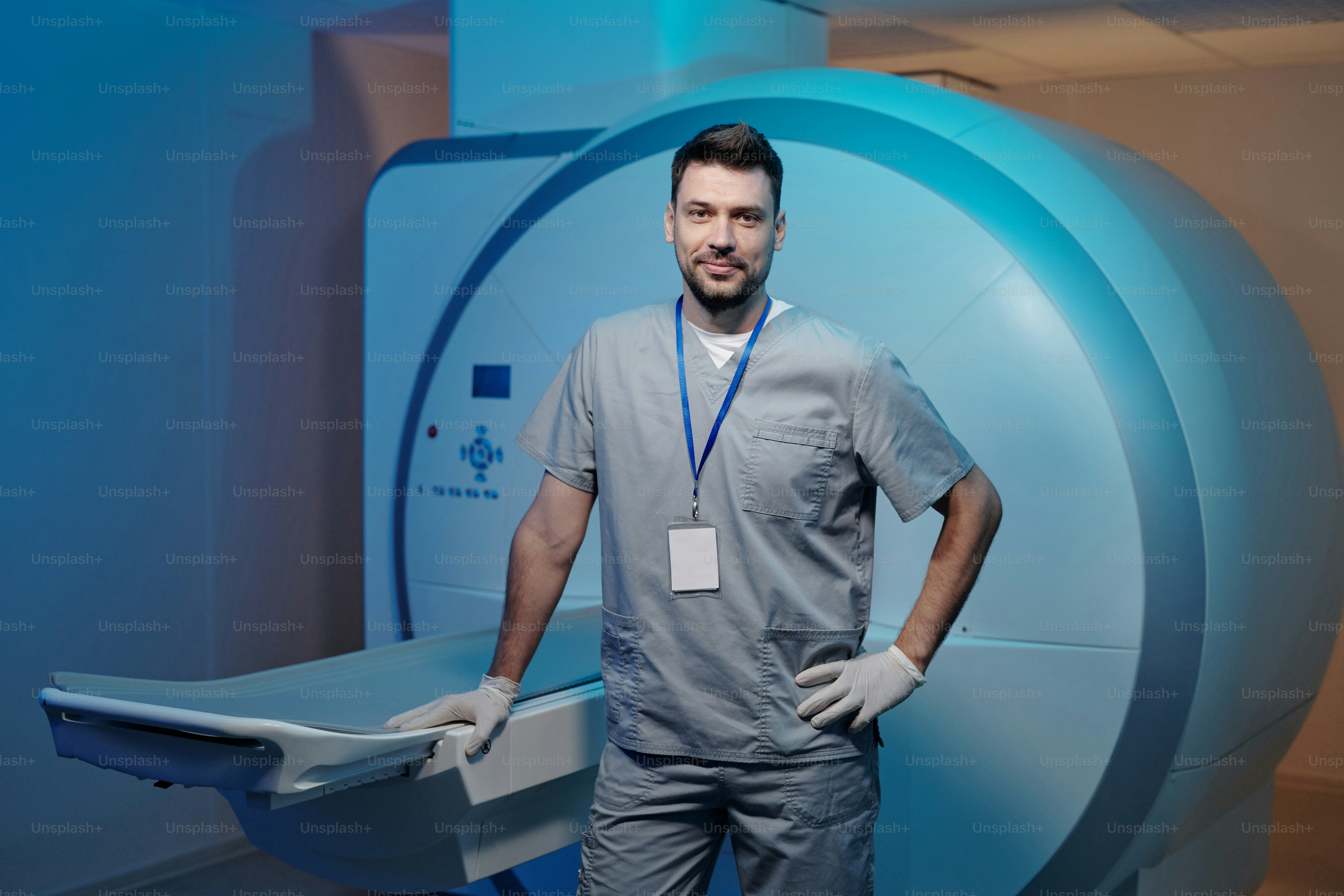 Médico seguro en uniforme gris de pie junto a la mesa del equipo de resonancia magnética en un laboratorio moderno