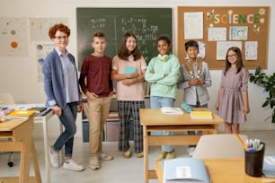 Young successful teacher and group of secondary school students standing against blackboards