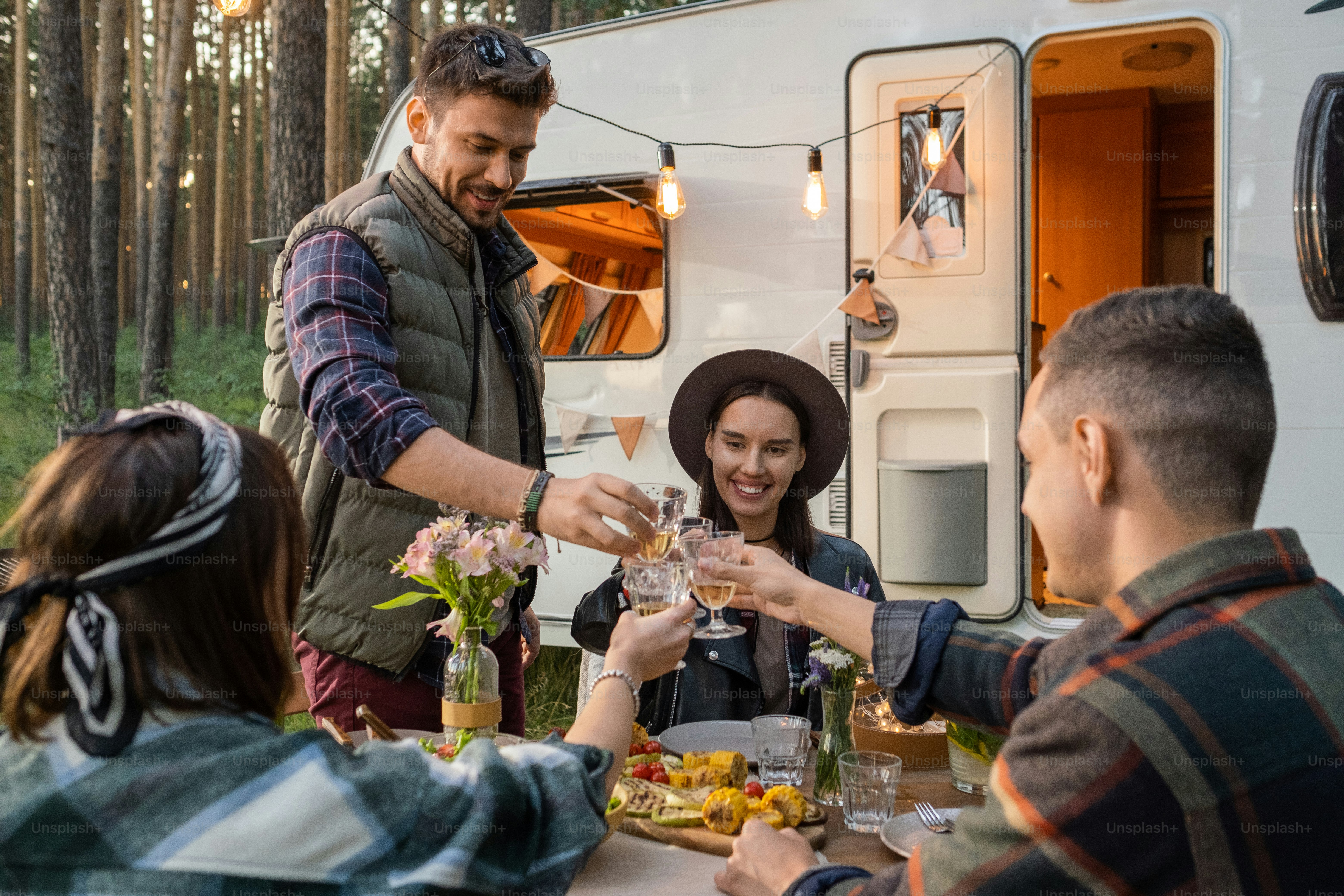 Happy friends clinking glasses of wine over served table while enjoying dinner by house on wheels