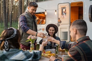 Happy friends clinking glasses of wine over served table while enjoying dinner by house on wheels