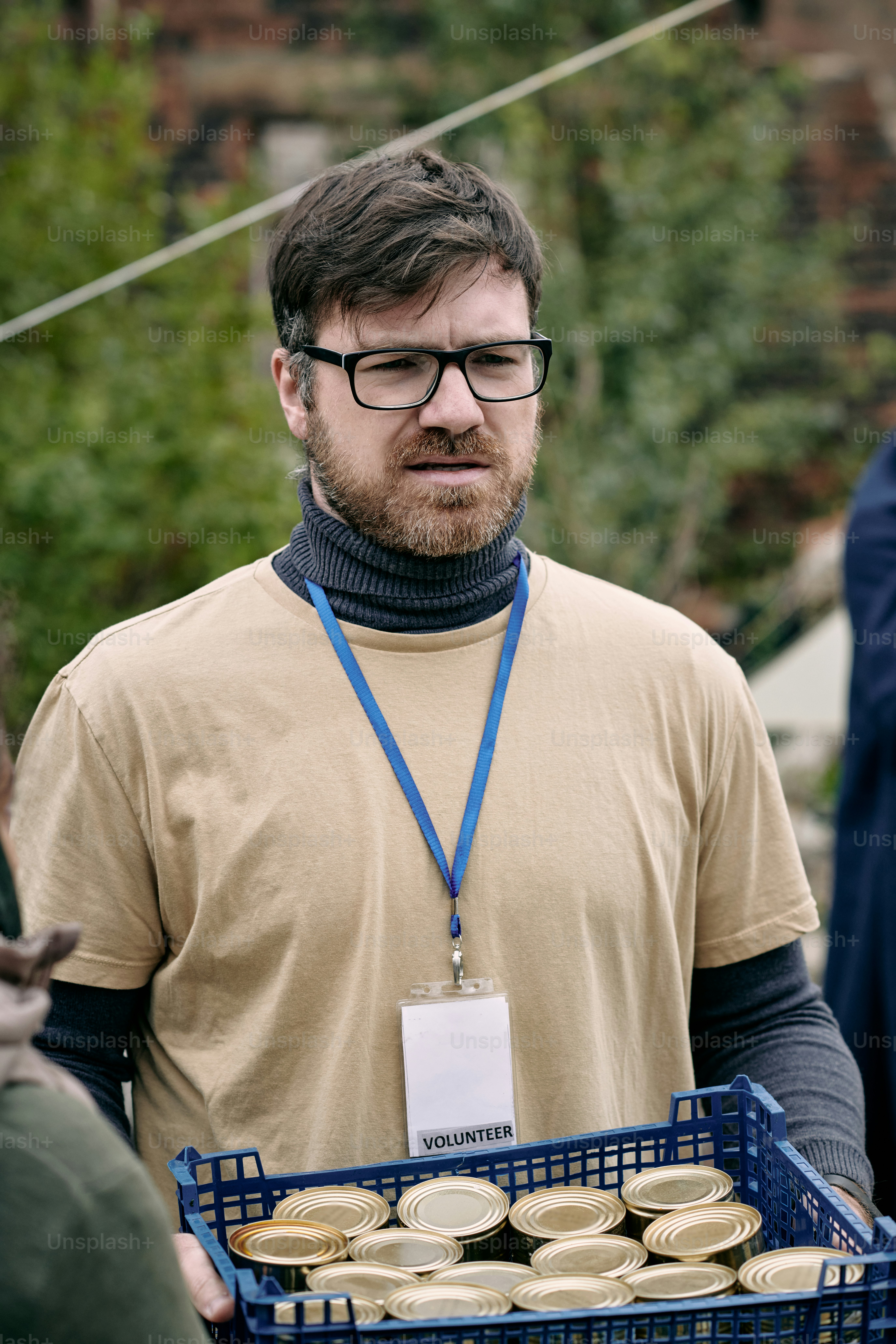 Empathetic male social worker with Volunteer badge carrying box of tin cans for refugees