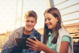 Adolescentes menina e menino no banco usando tablet digital, foco seletivo