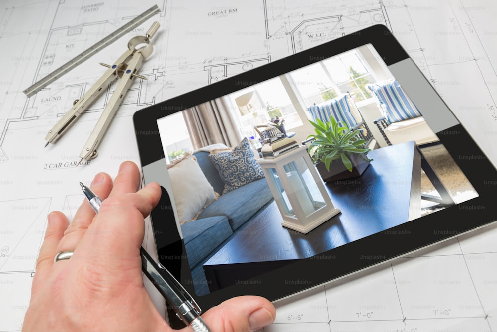 Hand of Architect on Computer Tablet Showing Home Interior Photo Over House Plans, Compass and Ruler.