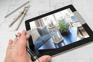 Hand of Architect on Computer Tablet Showing Home Interior Photo Over House Plans, Compass and Ruler.