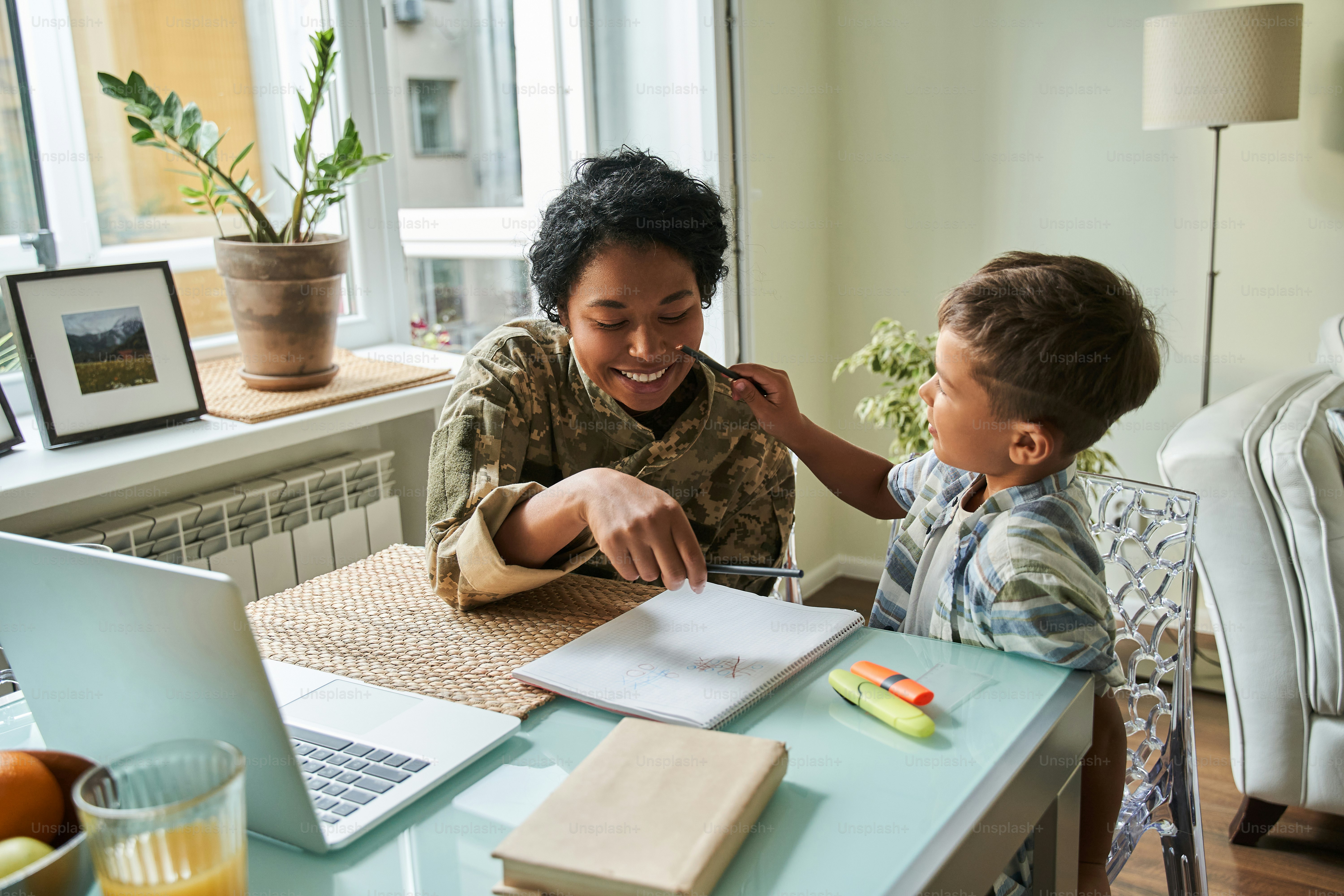 Menino engraçado sentado à mesa com sua adorável mãe vestindo uniforme militar enquanto conversam uns com os outros e discutem algo