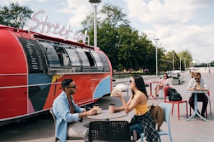 Casal jovem feliz interagindo pela mesa no café ao ar livre enquanto toma fast food e bebidas