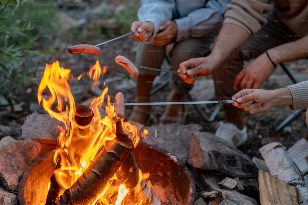 자연 환경에서 휴식을 취하는 동안 모닥불 위에서 소시지를 요리하는 세 명의 젊은 가족