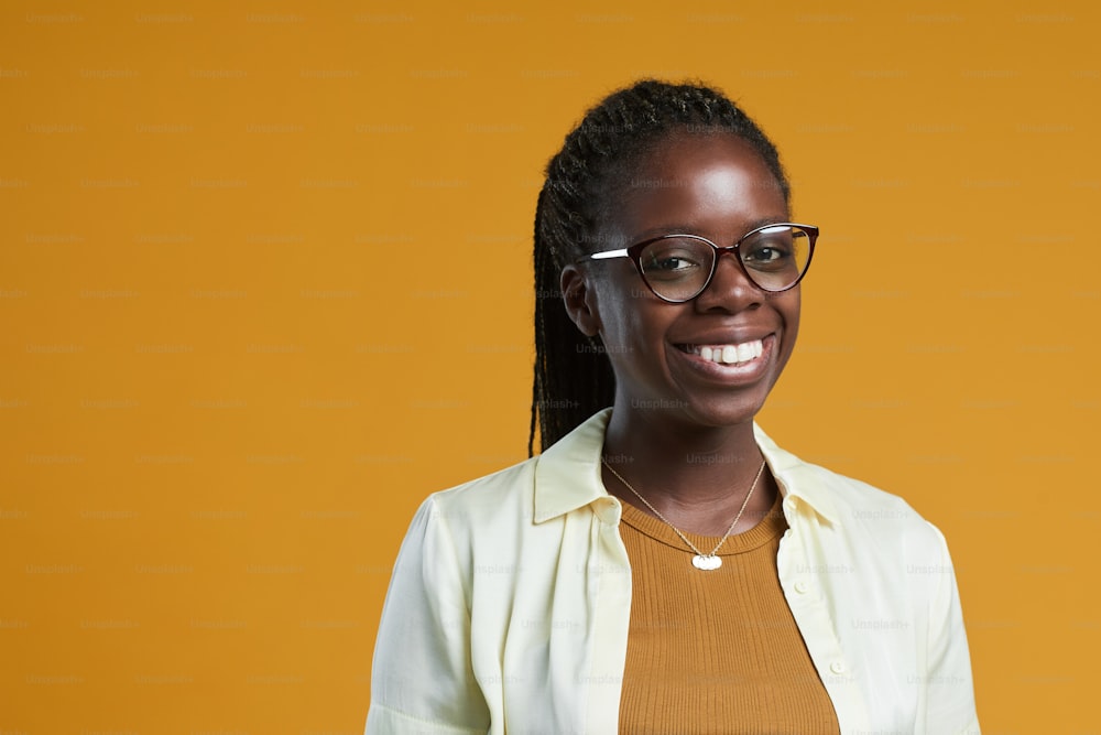 Porträt einer jungen afroamerikanischen Frau, die eine Brille trägt und in die Kamera lächelt, während sie vor gelbem Hintergrund im Studio posiert