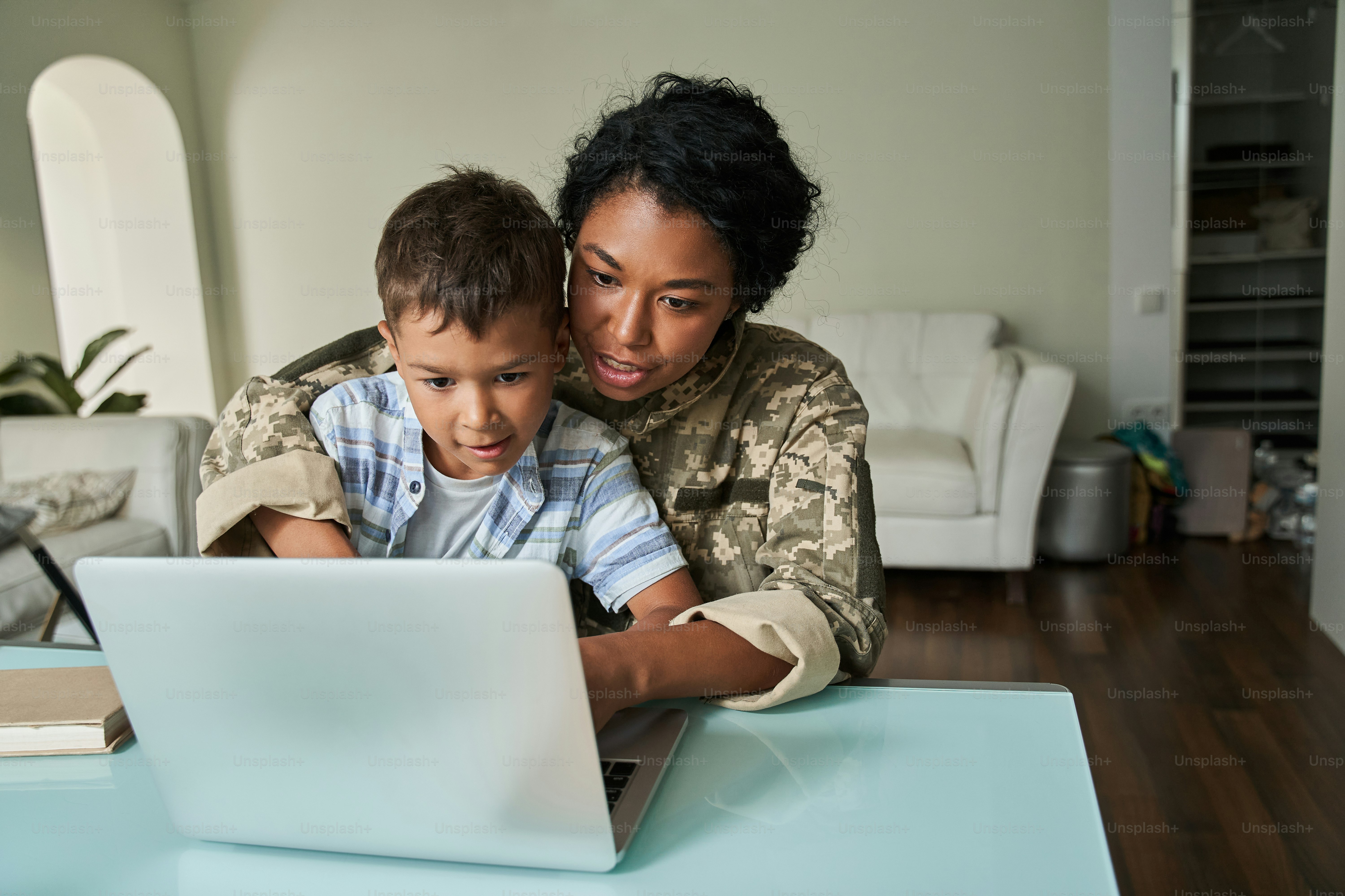 Tão interessante. Vista retrato do garotinho sentado nos joelhos de sua mãe militar e olhando para a tela do laptop juntos. Família passando fim de semana em casa
