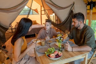 Family of three interacting by served table during breakfast in glamping tent