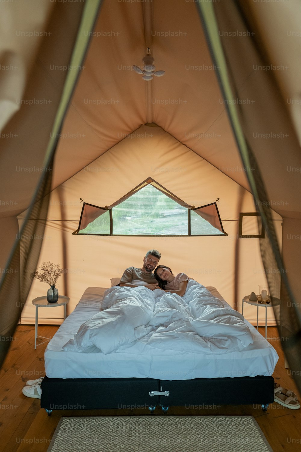 Young amorous couple resting in bed under white blanket in the morning inside glamping tent