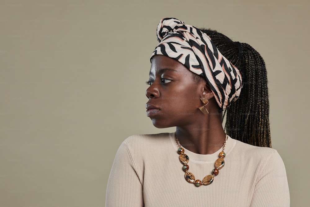 Retrato de vista lateral mínima de una joven afroamericana mirando hacia otro lado mientras usa accesorios étnicos y posa contra fondo beige marrón neutro, espacio de copia