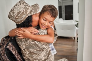 Waist up portrait view of the multiracial loving mom returning home to her child and kissing him with tenderness. Returning from war concept