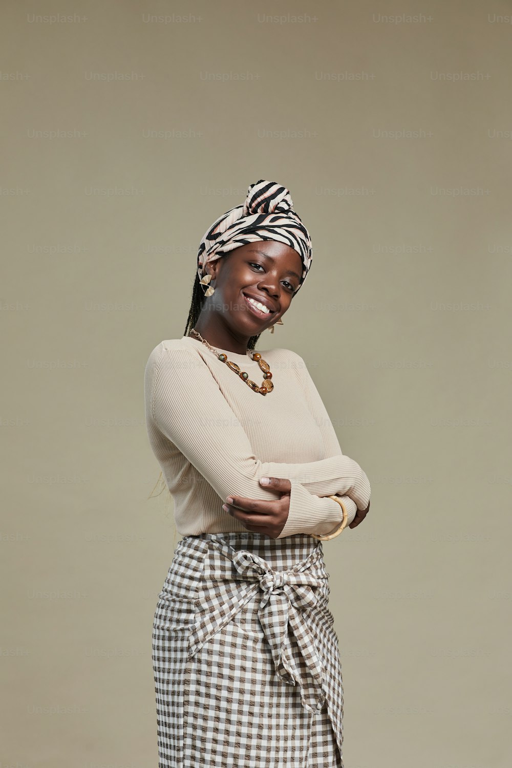 Retrato vertical de una joven afroamericana vestida con estilo étnico y sonriendo a la cámara mientras posa contra un fondo beige neutro en el estudio
