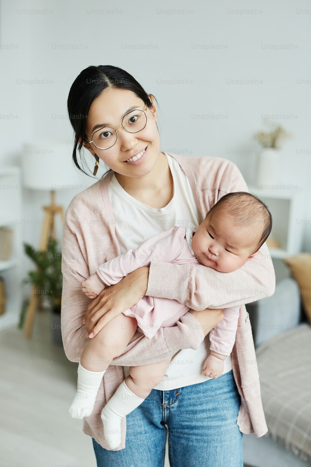 Portrait of Asian young woman smiling at camera while standing in the room and holding her little child