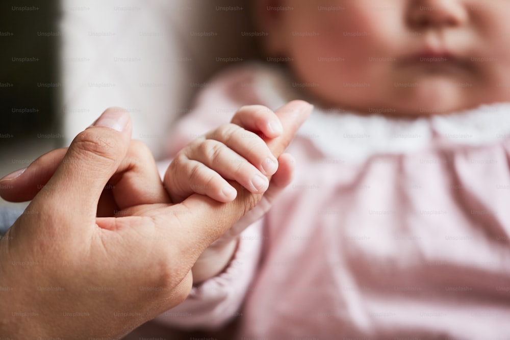 Close-up of newborn baby holding hand of her mother