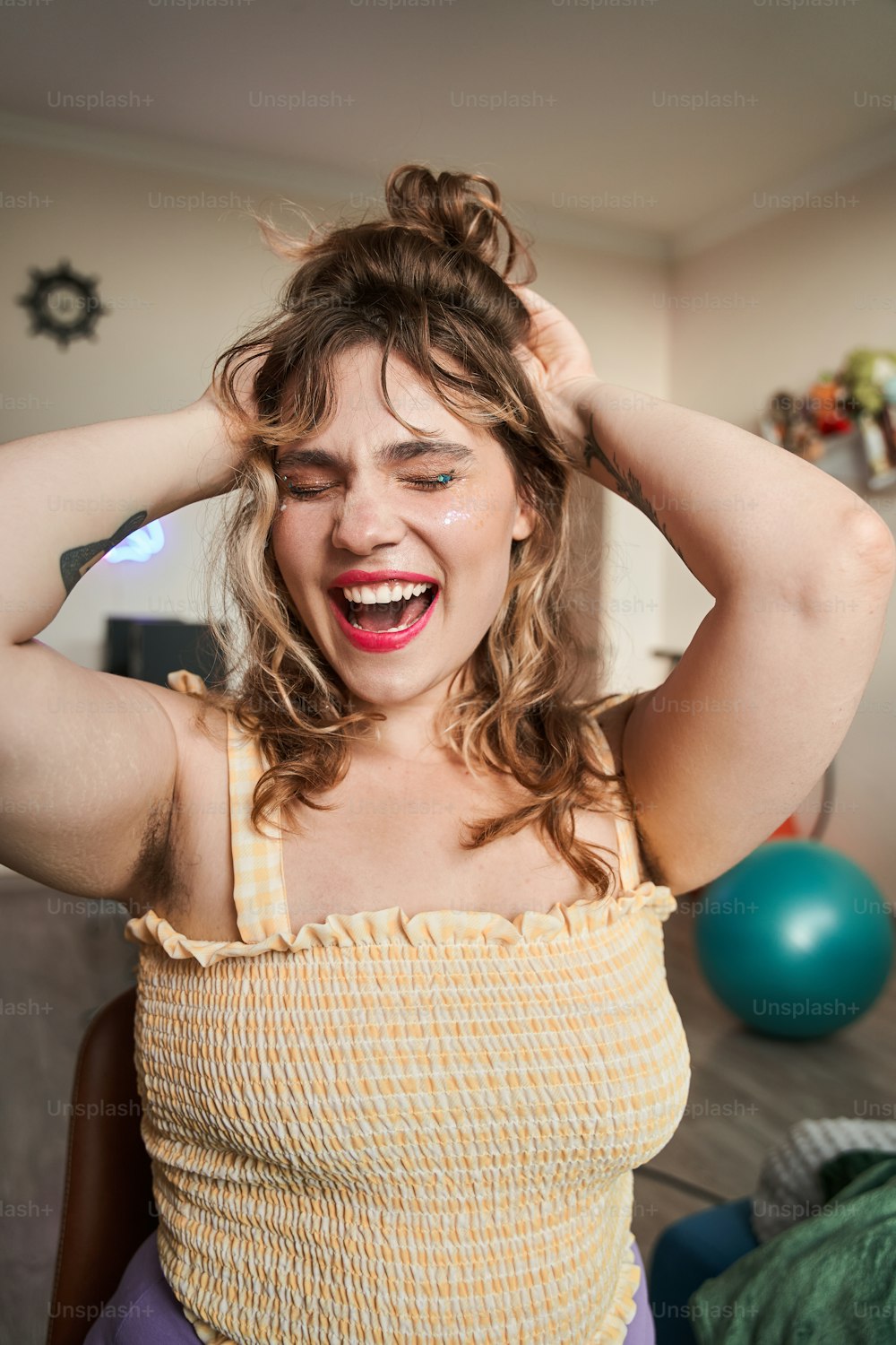 Oversize woman with closed eyes screaming and touching her hair at home. Concept of body positive. Idea of feminism. Domestic lifestyle. Young european girl with makeup, tattoo and unshaved armpits