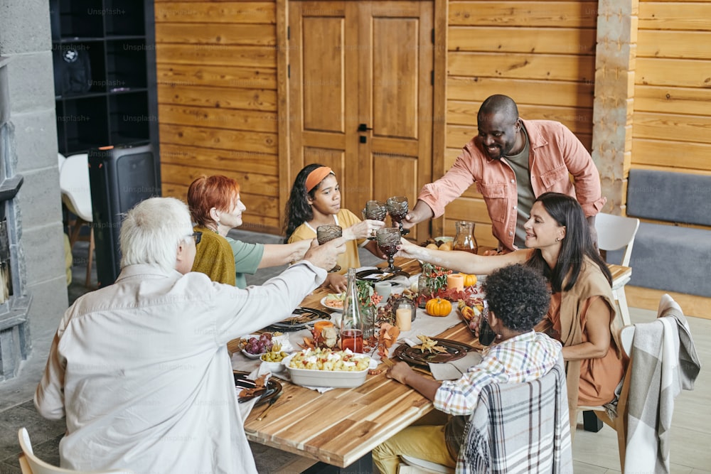 Gran familia brindando copas con bebidas mientras está sentado en la mesa del comedor durante la celebración