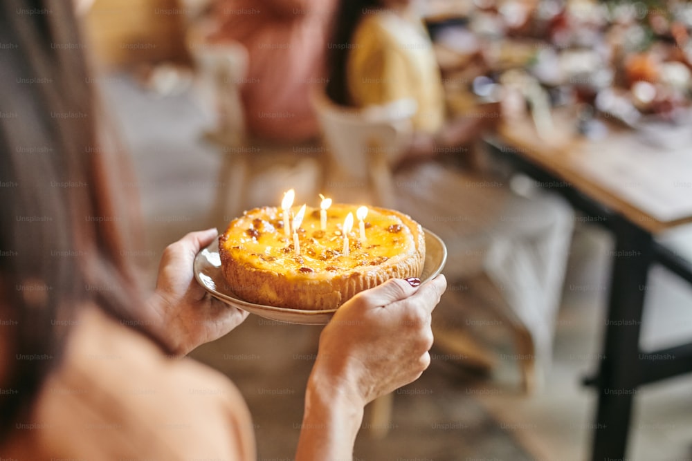 Close-up of woman carrying plate with homemade cake and candles to the table at the birthday party