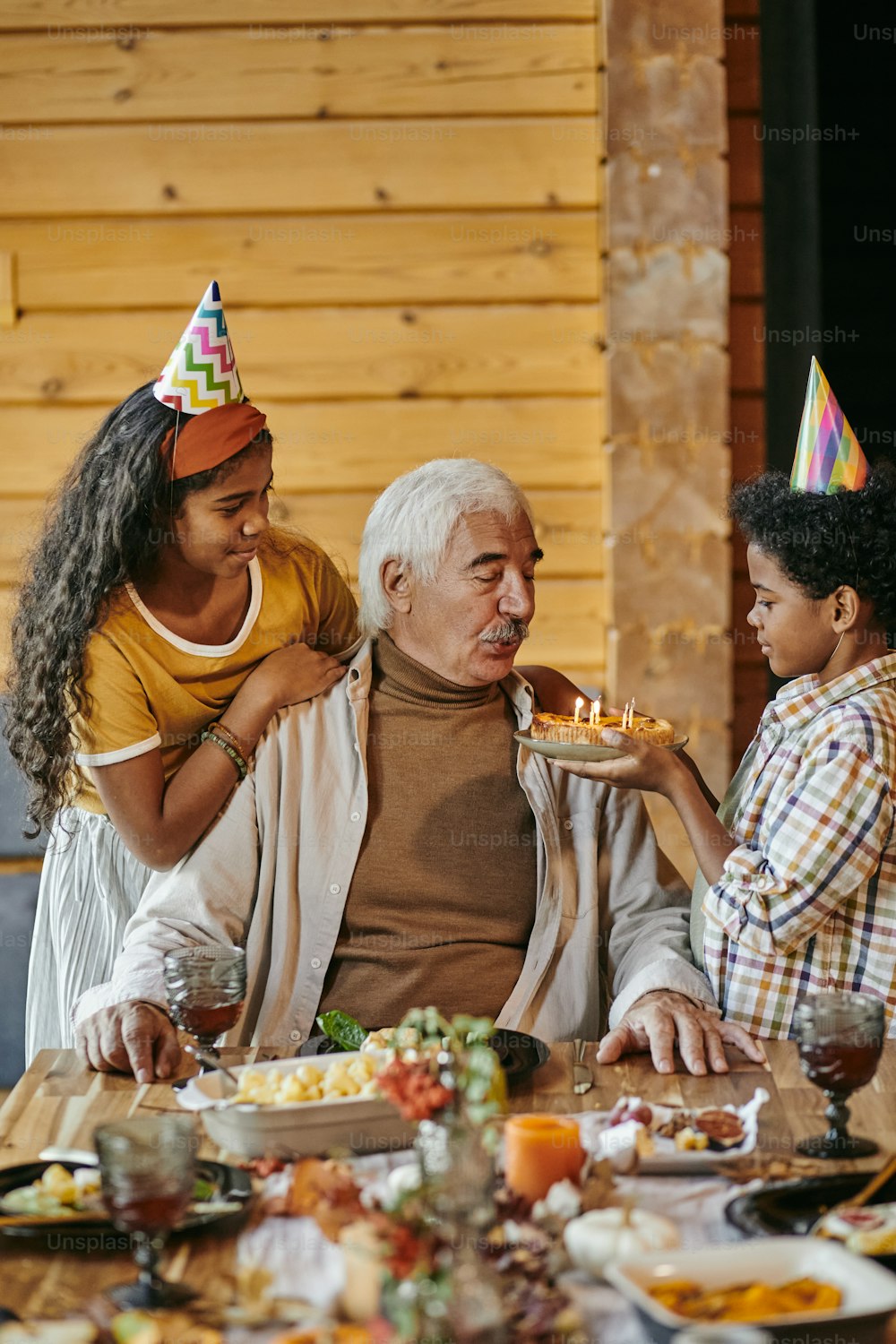 Abuelo soplando velas en el pastel mientras sus nietos lo felicitan con el cumpleaños