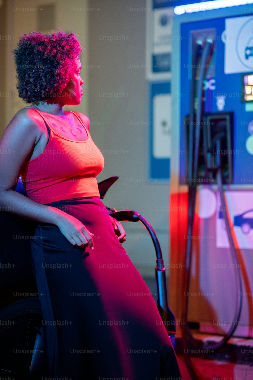 Young elegant woman standing by electric car at station during charge process