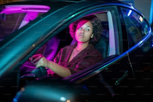 Joven afroamericana conduciendo un automóvil eléctrico mientras sostiene el volante