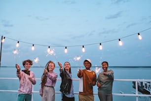 Happy young multiracial people with sparkling bengal lights enjoying outdoor party on pier