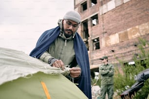 Männlicher Flüchtling schlägt Zelt im Lager für Migranten gegen halb zerstörtes Gebäude auf