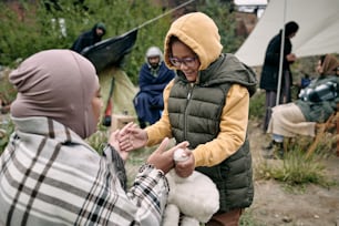 Happy little girl playing with young woman in hijab against their family in asylum for refugees