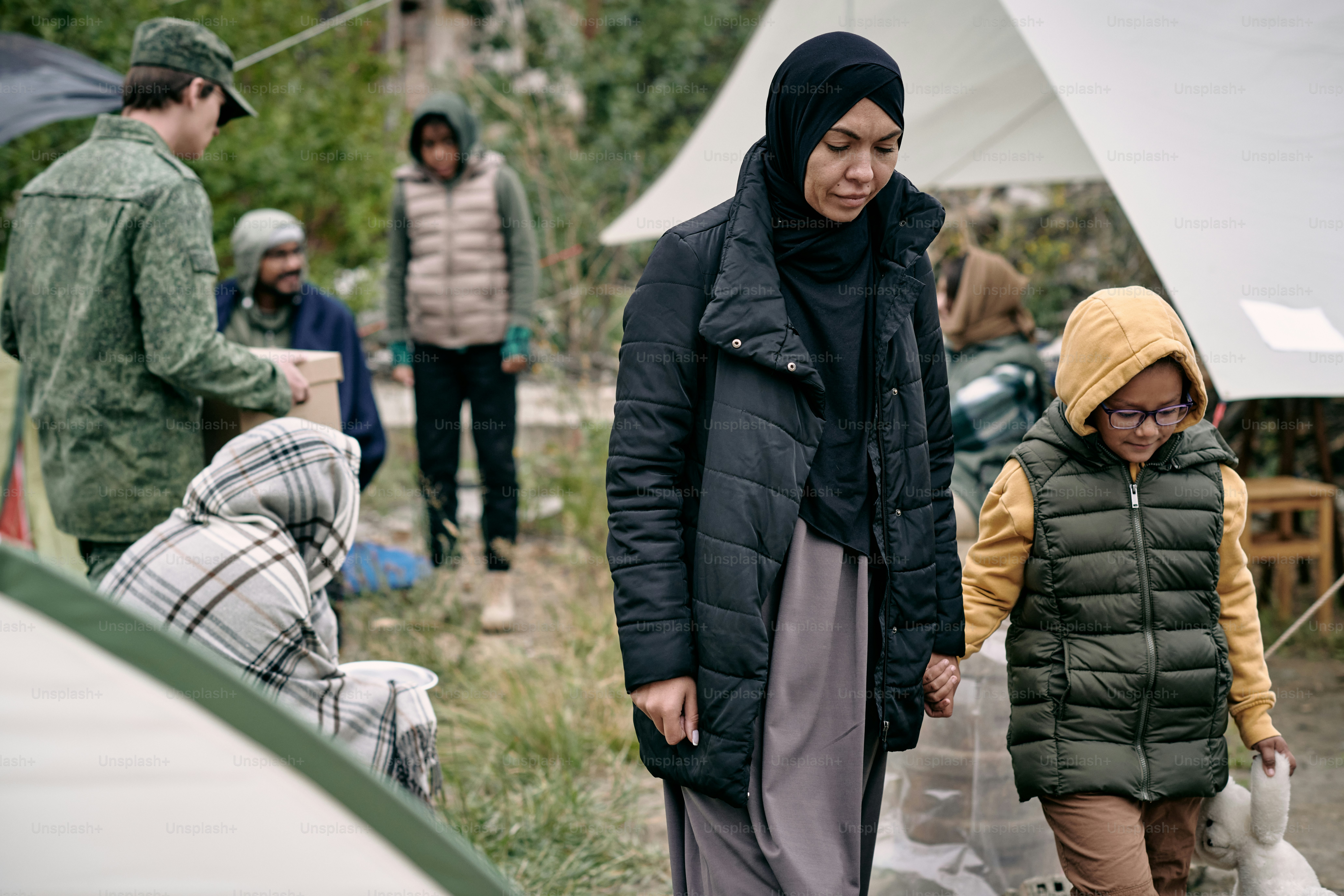 Young Muslim female holding her little daughter by hand while moving along refugee camp