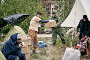 Young volunteer and representative of migration service spreading donation among refugees in camp