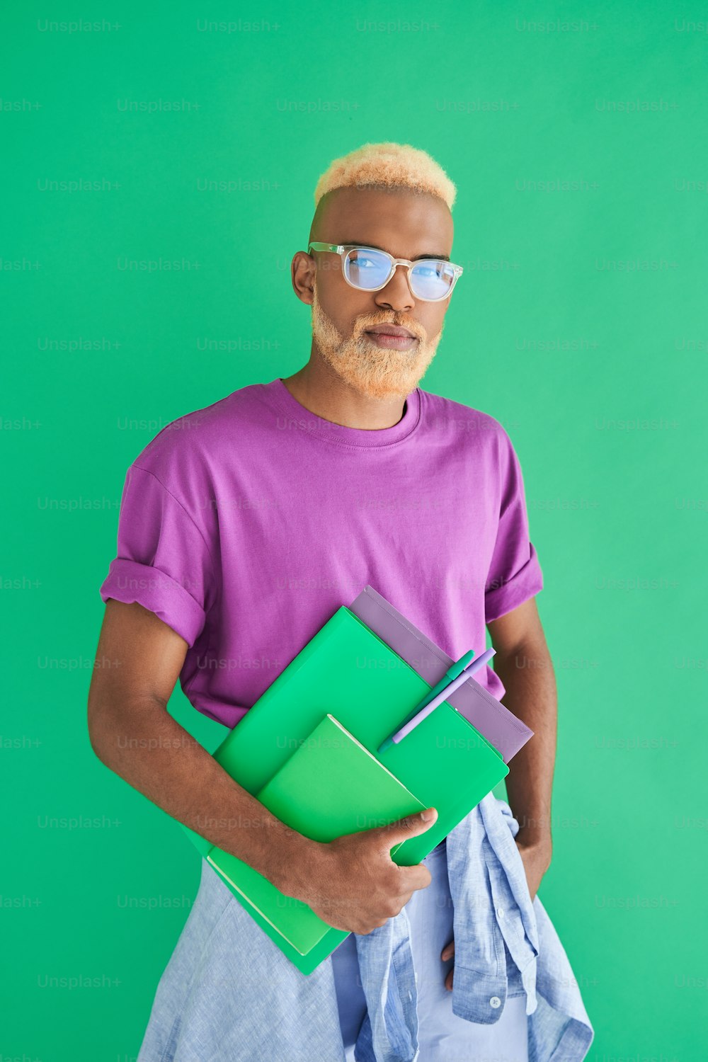 Going to the work. Vertical shot of the multiracial blonde man wearing glasses holding folders and notebook while posing over the green wall