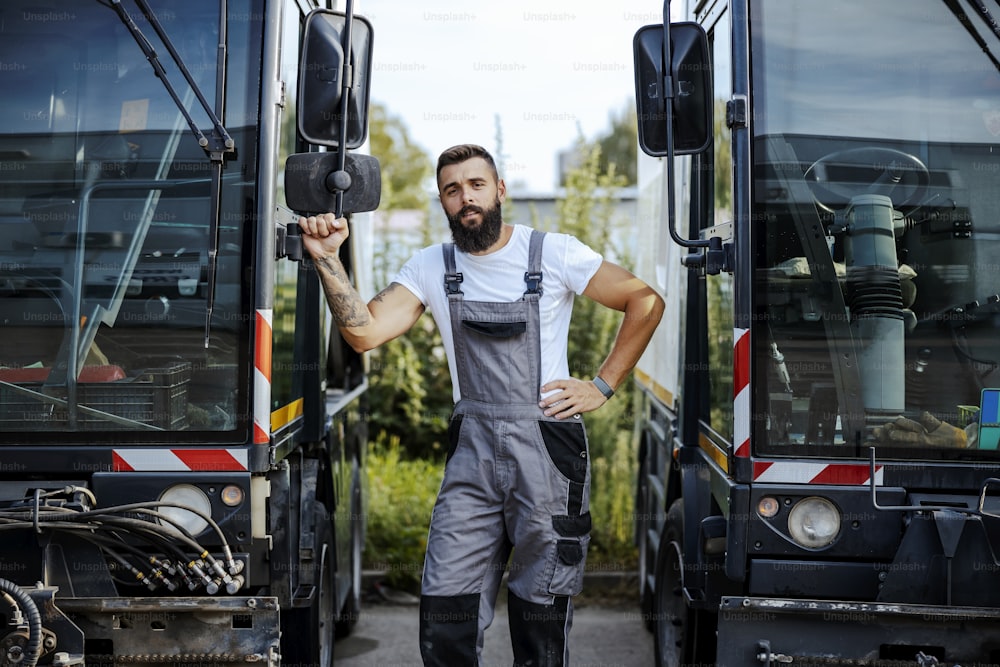 A hardworking auto-mechanic standing outdoors and leaning on the bus. Auto-mechanic doing work in a car factory. Worker with buses.