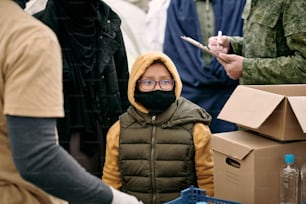 Bambino in maschera protettiva e la sua famiglia in attesa di diffondere cibo gratuito da parte dei volontari