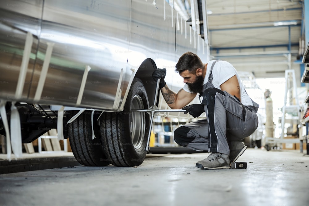 An auto-mechanic crouching next to a car wheel and replacing a tire. He is using special tools. Auto-mechanic in workshop
