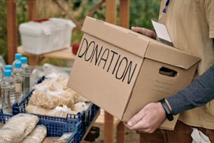 포장된 기부 상자를 들고 있는 남성 자원봉사자는 무료 음식이 있는 테이블 옆에 서 있다