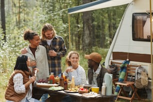 Diverse group of young people enjoying picnic outdoors while camping with trailer van