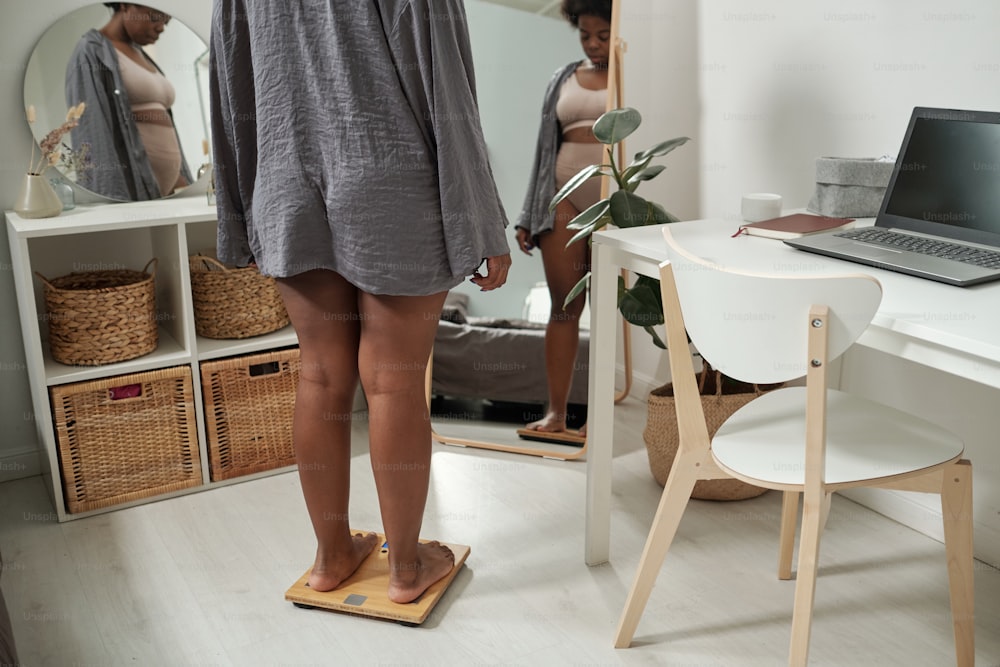 Young plus size woman in grey shirt checking her weight while standing on scales