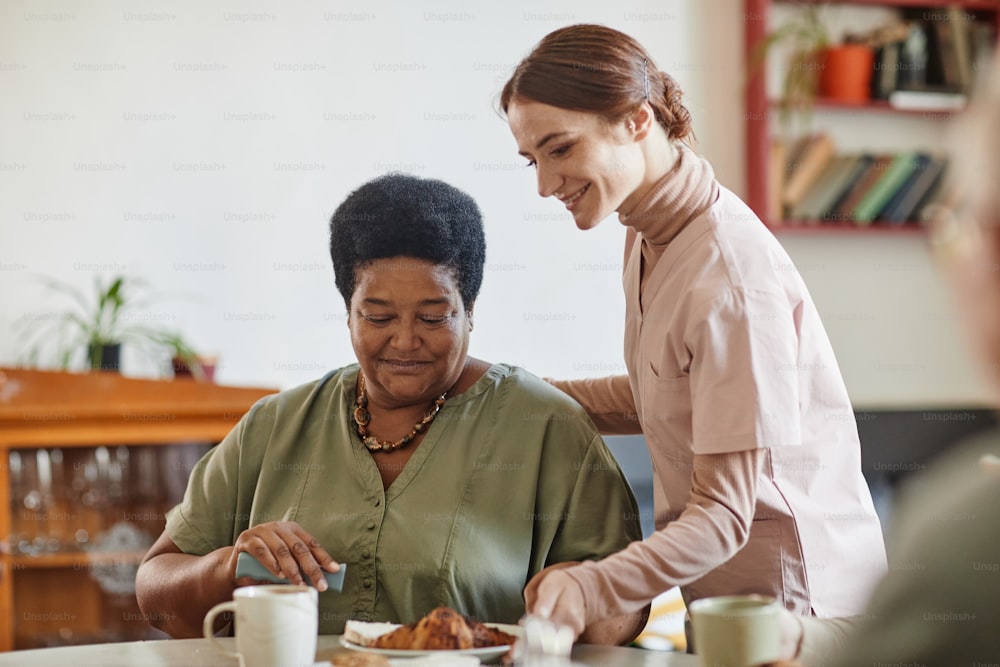 Portrait of smiling young woman caring for senior African-American lady in nursing home, copy space