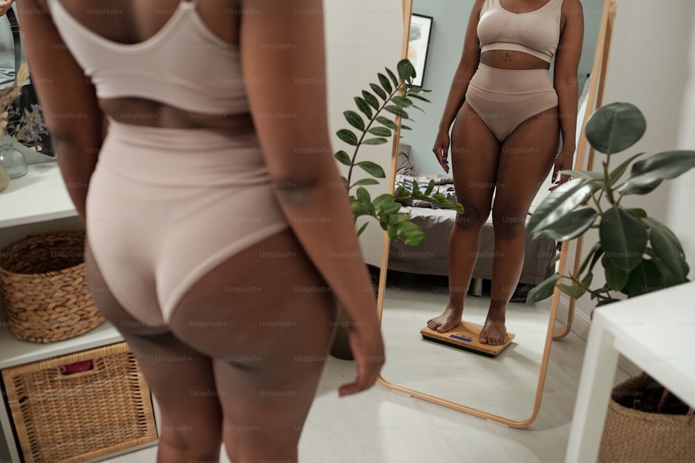 Mulher plus size de cueca verificando seu peso na balança em frente ao espelho grande