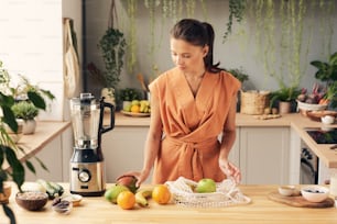 Junge Hausfrau, die frisches Obst zubereitet, während sie im elektrischen Mixer einen Smoothie zubereitet