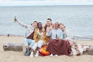 Full length portrait of diverse group of friends enjoying camping on beach in Autumn and posing for photo
