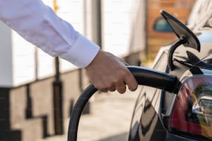 Hand of young man charging his new electric car at station while holding plugged charger