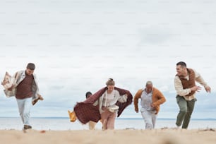 Candid shot of young people running on beach in Autumn and having fun together outdoors