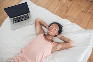 Morning at home. A young woman lying on bed, laptop next to her