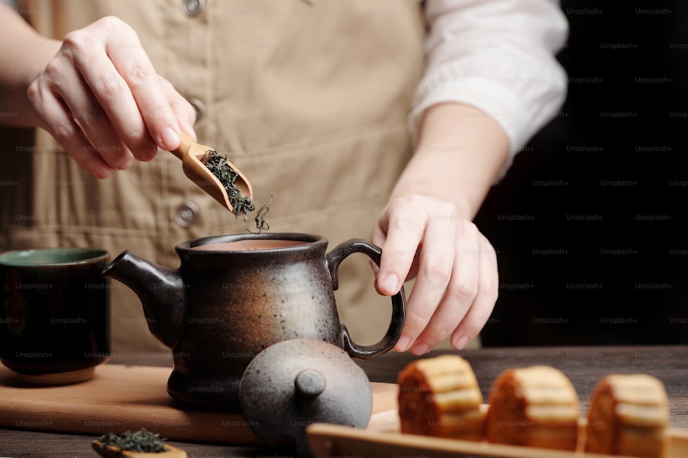Mann fügt getrocknete grüne Teeblätter in Keramikkanne hinzu, wenn er Getränke für das Mittherbstfest zubereitet
