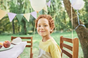 Portrait d’un garçon souriant regardant la caméra à une table de pique-à l’extérieur profitant d’une fête d’anniversaire en été