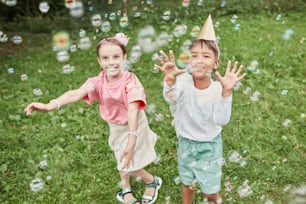 Retrato de comprimento completo de duas meninas bonitas brincando com bolhas enquanto desfruta da festa de aniversário ao ar livre no verão